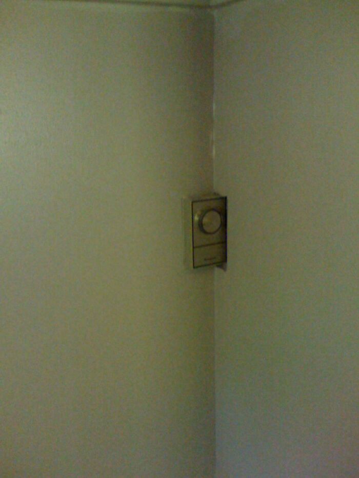 A thermostat awkwardly installed in the corner where two walls meet, illustrating a DIY fail.
