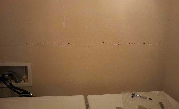 A wall with many small holes in an uneven line, showing a DIY fail from someone whose confidence outpaced their skills.