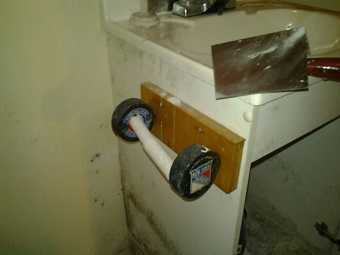 A DIY toilet paper holder made from hockey pucks and a wooden plank, a clear DIY fail.