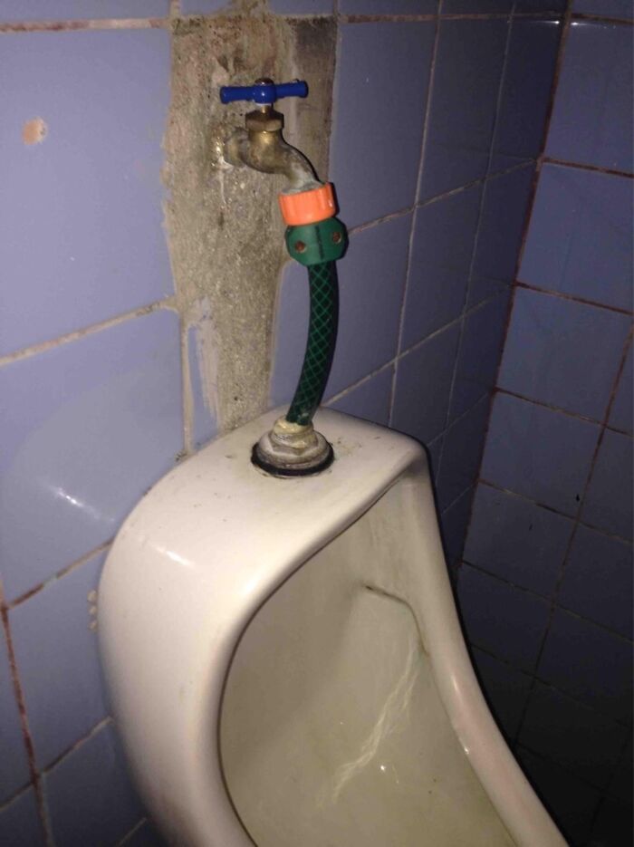 A garden hose connected to a faucet in a urinal, an epic DIY fail.