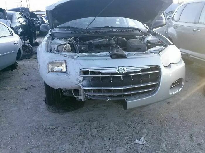 A silver car with a severely damaged front bumper and an exposed engine, showcasing a significant DIY fail.