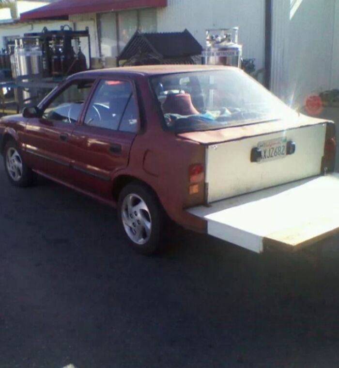 A red car with a wooden extension, showing a significant DIY fail.