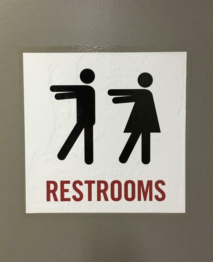A chaotic sign for restrooms with male and female figures seemingly pushing each other, spotted in the wild.