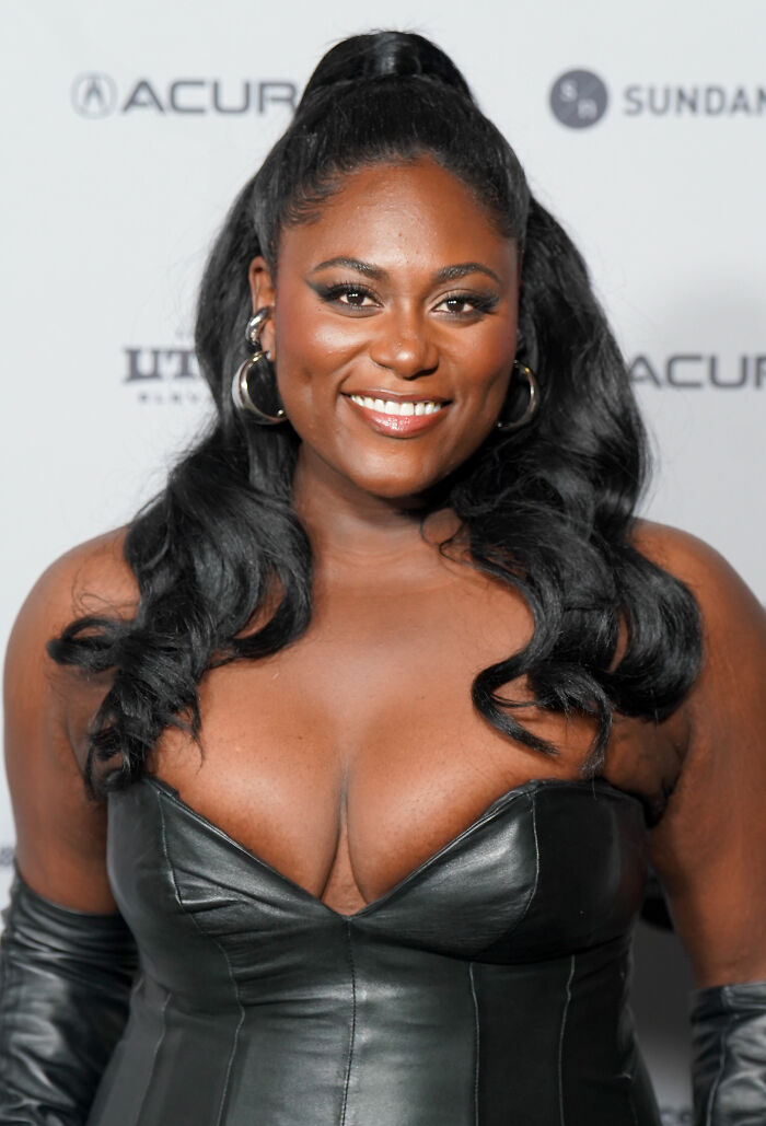Danielle Brooks smiling in a black leather dress, showcasing her career highlights and bio.