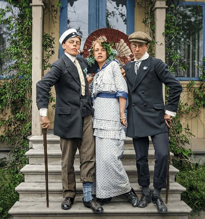 Historical colorized photo of three young people in early 20th-century attire posing on steps.
