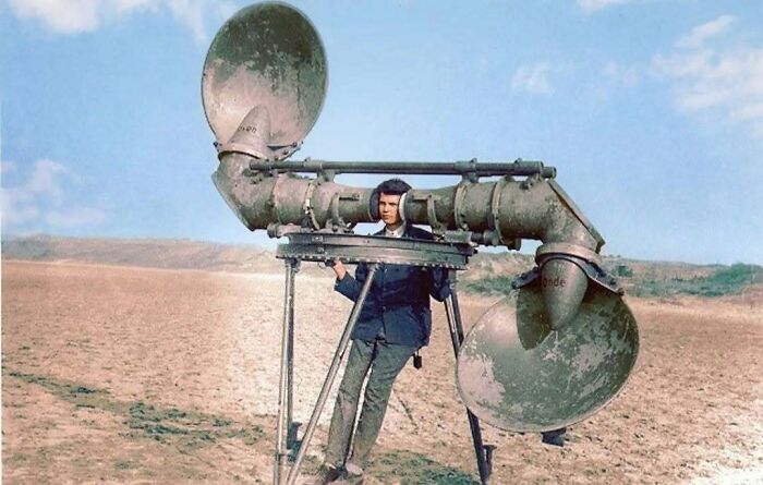 Historical colorized photos: Man with a large listening device in a barren landscape.