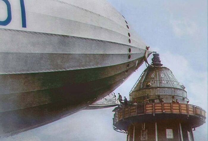 A historical colorized photo of a large airship moored to a tower, making the past come to life.