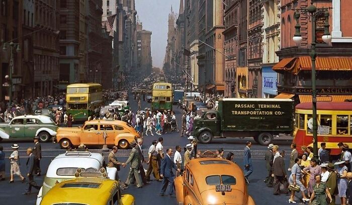 A busy street scene with cars, buses, and pedestrians, illustrating a historical colorized photo of urban life.