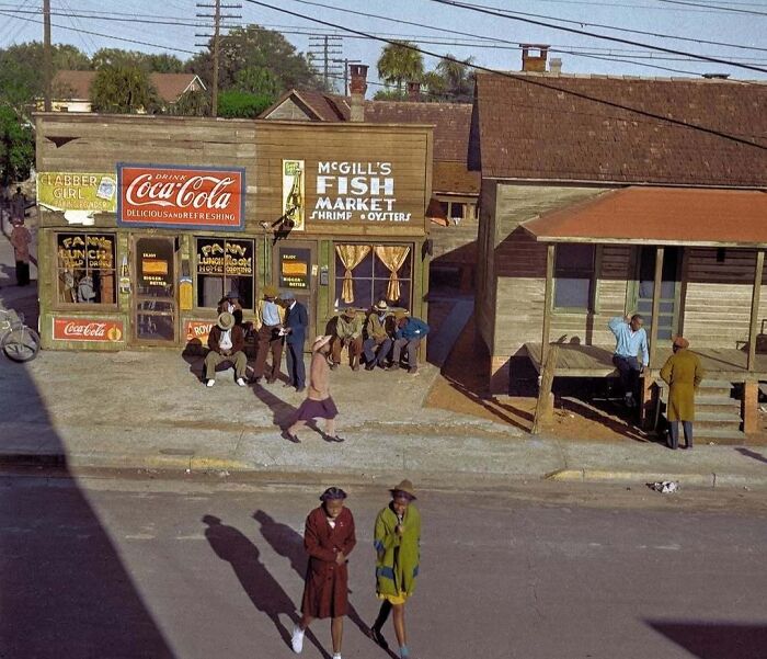 A vibrant historical colorized photo shows a lively street scene with shops and people, bringing the past to life.