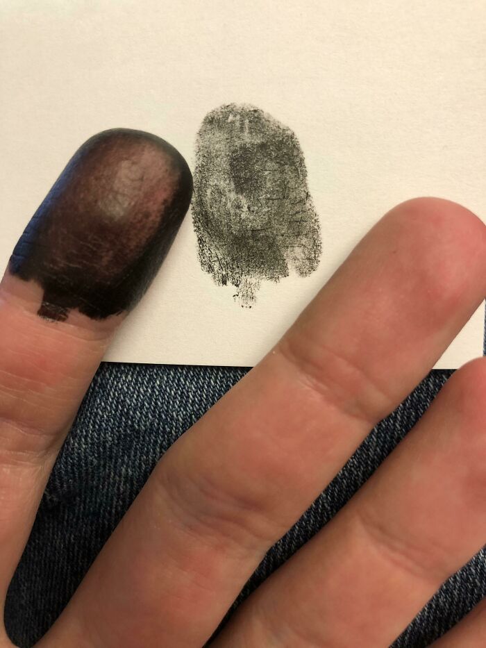 Finger covered in dark ink with corresponding fingerprint on paper