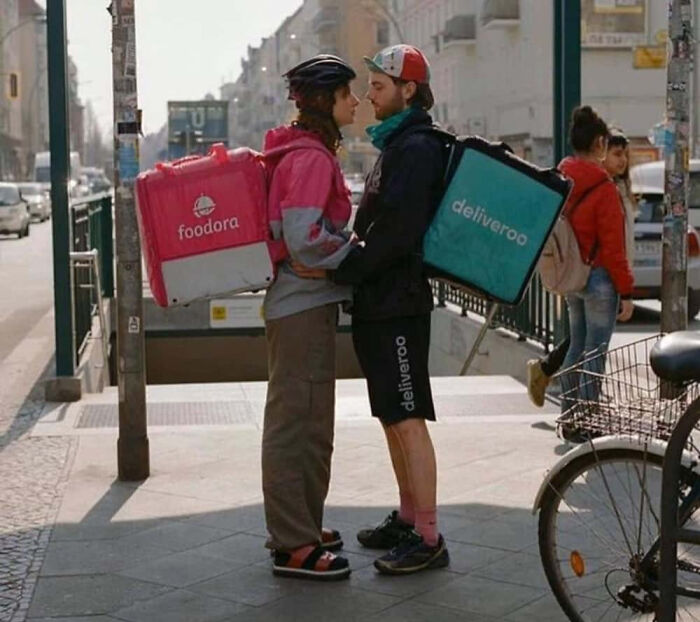 Hilarious photo of two food delivery drivers, one Foodora and one Deliveroo, sharing a kiss, embodying internet humor.