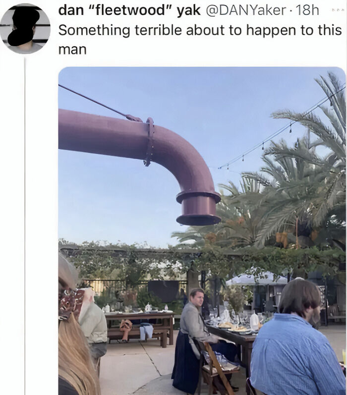 A man looks at the camera while a giant curved pipe is above his head, ready to drop on him, a hilarious photo.