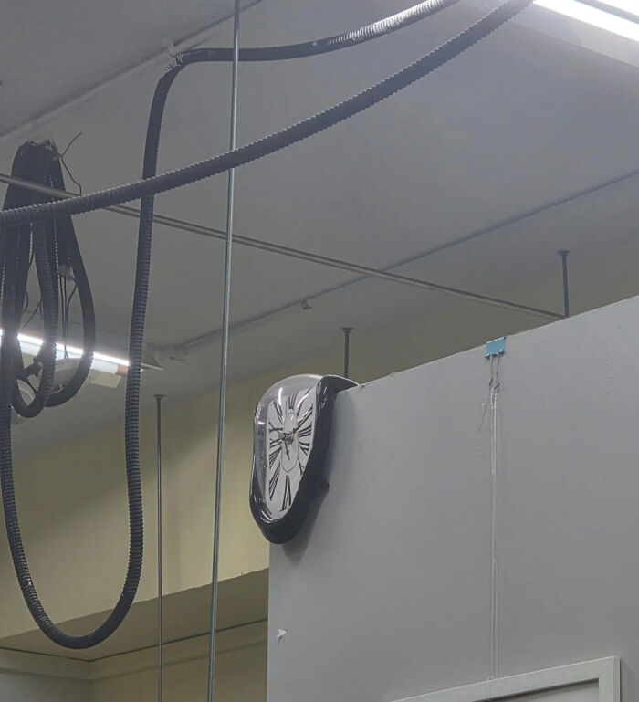 Hilarious photos: A melting clock hanging over the edge of a wall in a room with exposed ceiling pipes.