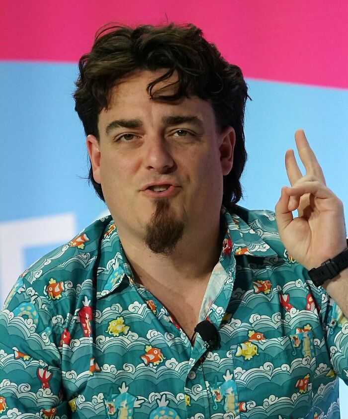Palmer Luckey in a colorful shirt, gesturing with his hand, discussing his career highlights.