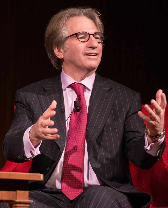 Barry Scheck, a legal expert, animatedly discusses career highlights, wearing a pinstriped suit, red tie, and glasses.