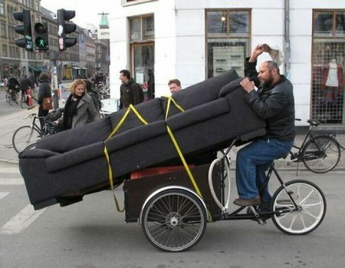 Man transporting large couch on tricycle in busy city street
