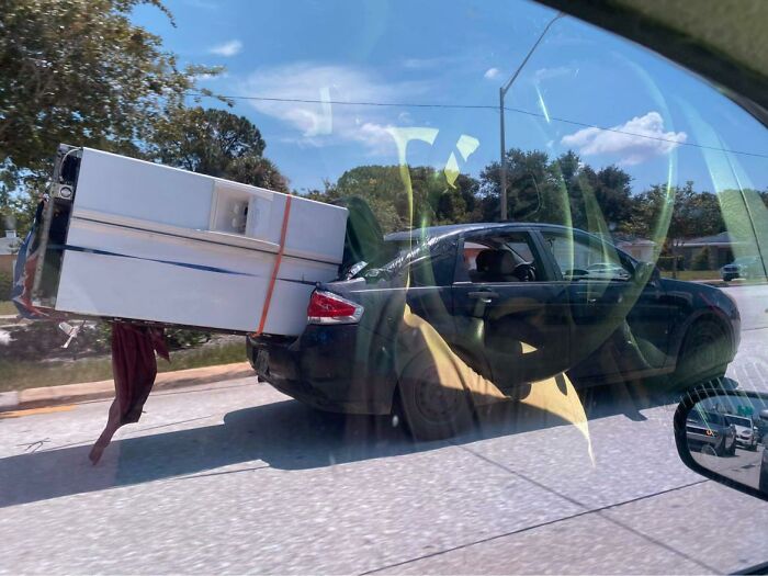 Car transporting a large refrigerator precariously strapped, a clear moving fail