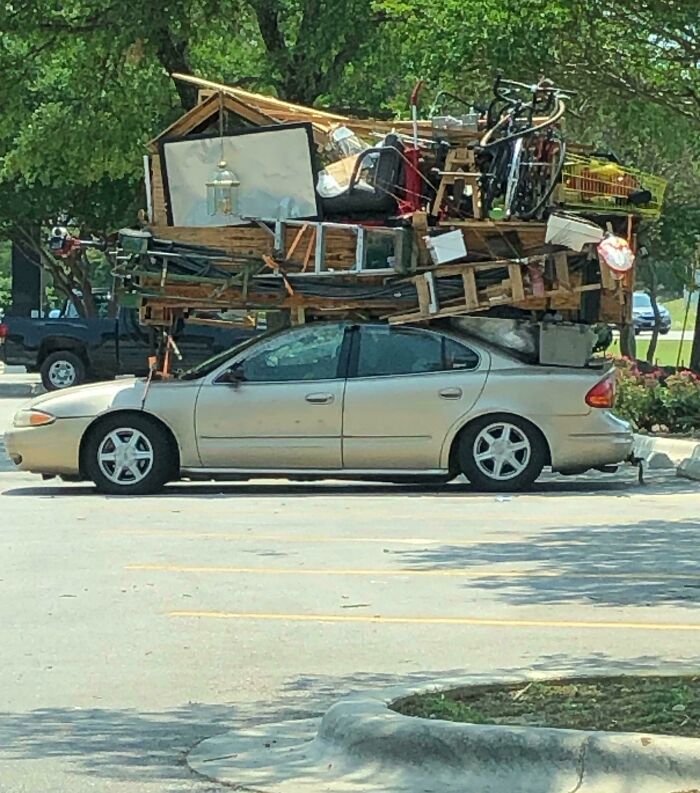 Car carrying excessive bulky items stacked high on roof, illustrating a moving fail