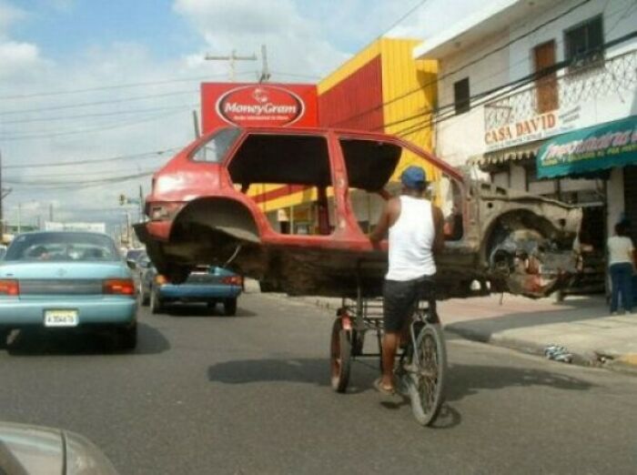 Person transporting empty car shell on bicycle, a funny moving fails moment.