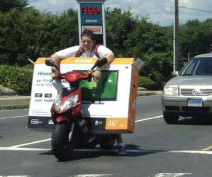 Moving fails photo of person awkwardly carrying large TV box while riding scooter
