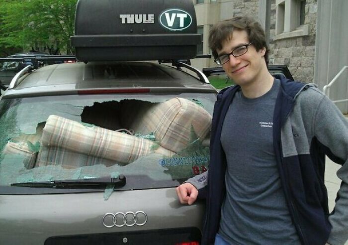 Moving fails image of man smiling next to car with smashed rear window from moving couch