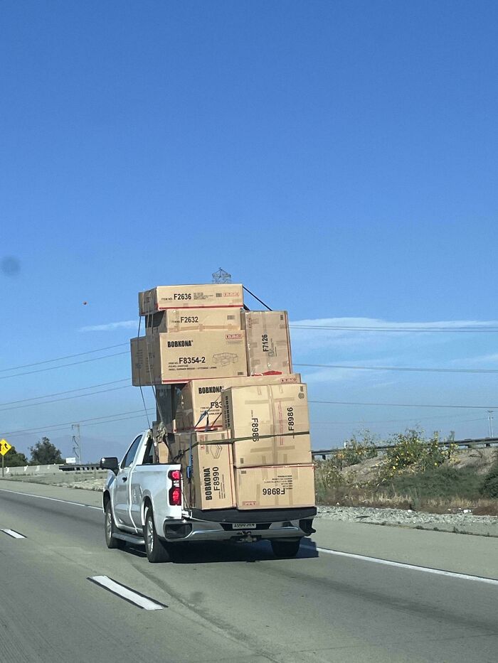 Truck carrying extremely tall stack of large moving boxes on highway