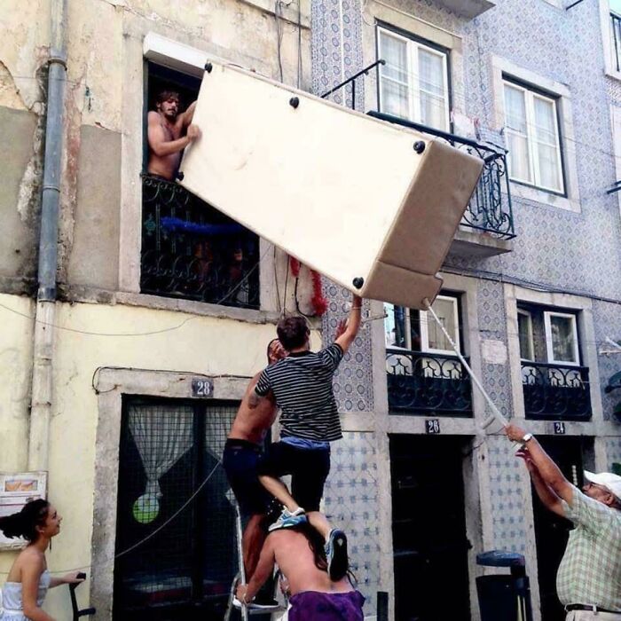 People struggling to move a large couch out of a window in a moving fails scenario