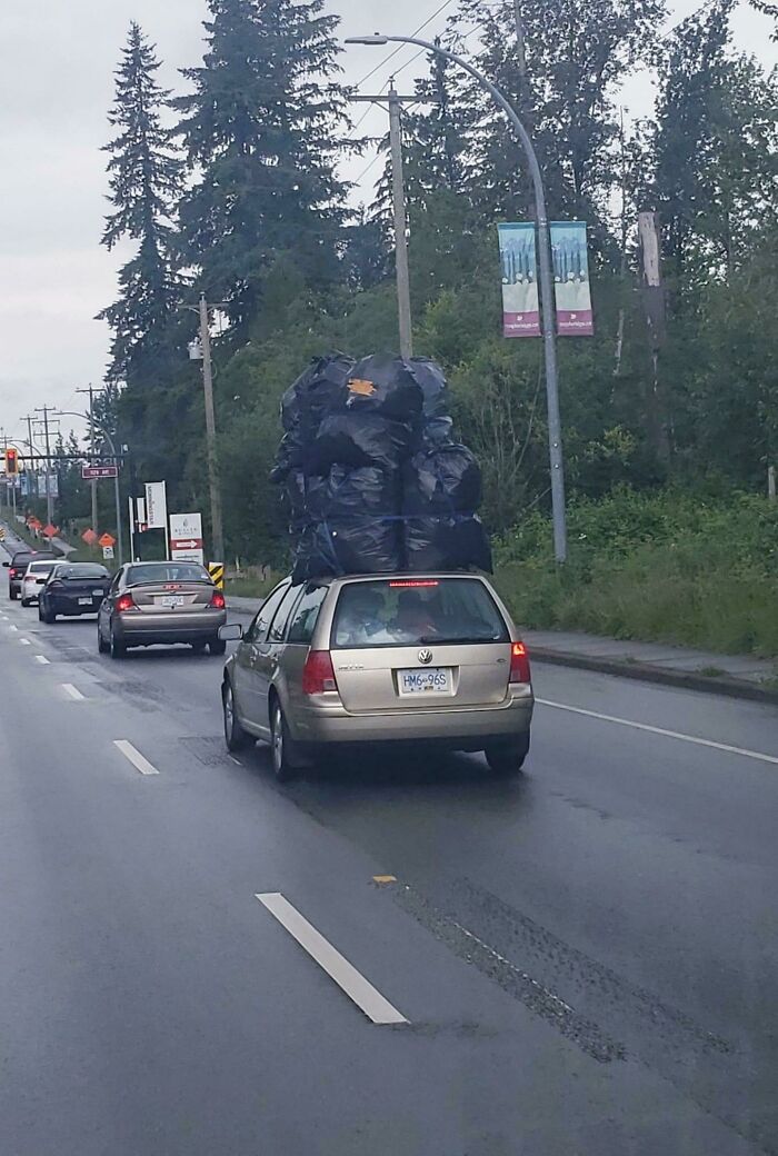 Car moving fail with large pile of black bags unsecured on roof