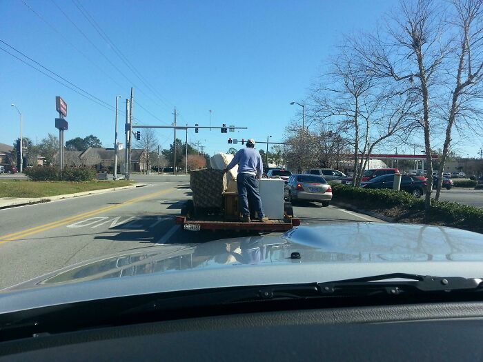 Man standing on trailer loaded with furniture on busy city road