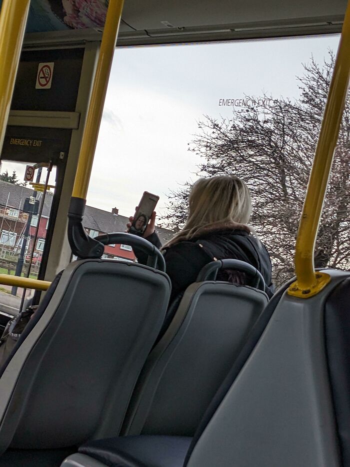 A passenger holding up her phone on a bus, capturing typical public transport interactions