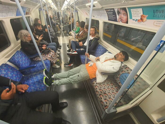 Man lying down with feet on handrail showing annoying public transport interactions on a subway train