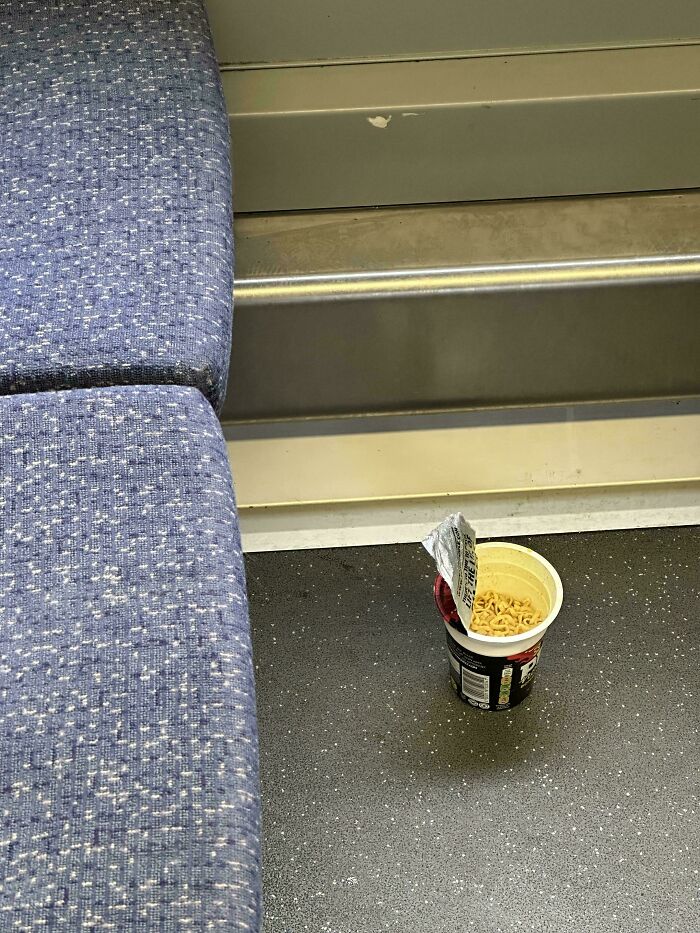 Leftover cup of instant noodles on a train floor, highlighting poor public transport interactions.