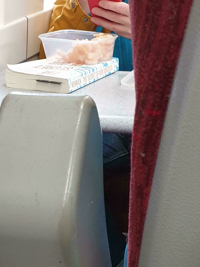Strange public transport interactions where a commuter has a plastic tub of prawns on a book