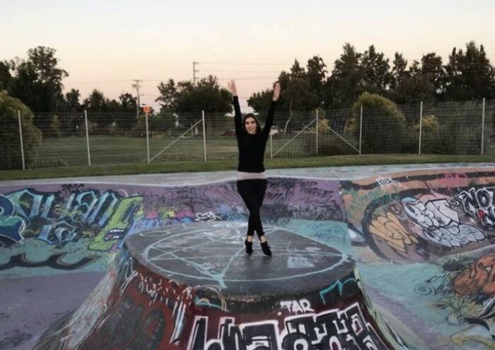 A woman standing with her arms raised in a graffiti-covered skatepark, creating an optical illusion.