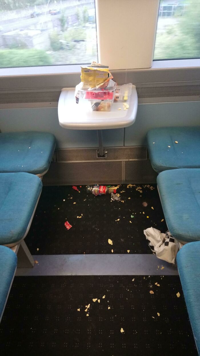 Trash and crumbs scattered all over train seats and floor, an unpleasant public transport scene.