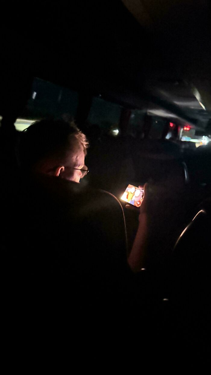 A passenger watching a bright screen on a dark bus, demonstrating public transport interactions.