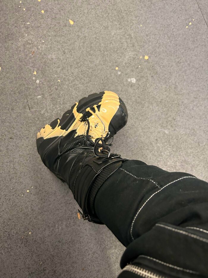 A black boot covered in yellow mustard, highlighting a wild public transport mishap.