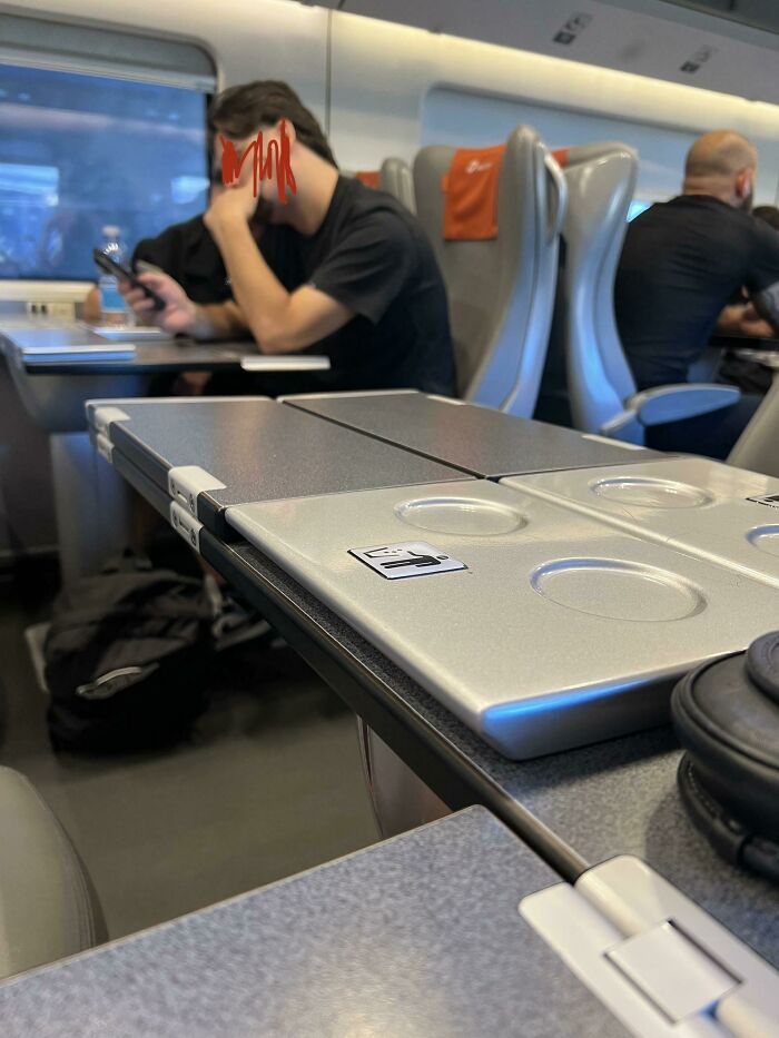 Man on public transport blocking multiple fold-down seats with his laptop setup
