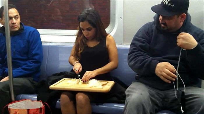 A woman slicing onions on a cutting board during a busy public transport ride on the subway