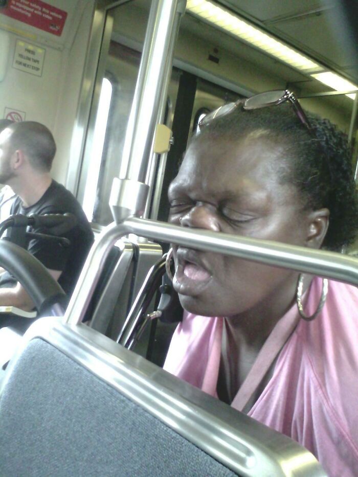 A sleeping passenger with her face pressed against a metal bar in a public transport train