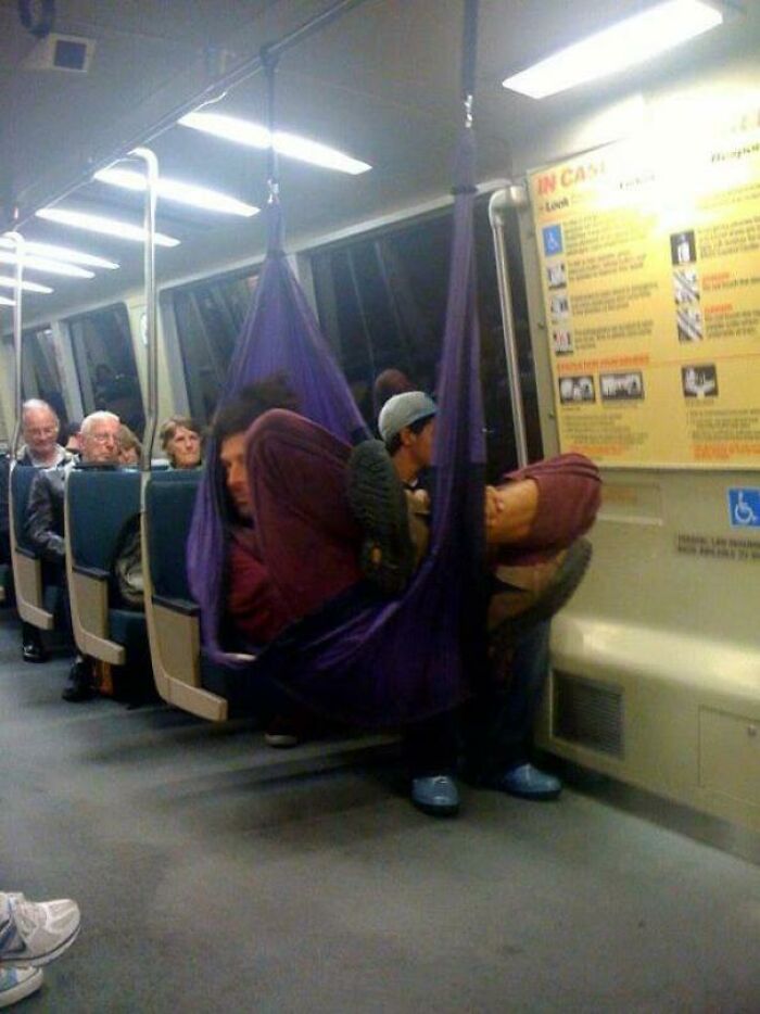 A passenger sleeping in a purple hammock hung from the ceiling rails in a public transport carriage