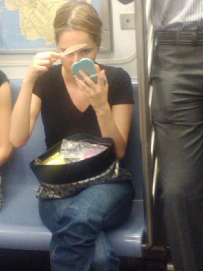 A woman spreading butter on her forehead using a knife, capturing bizarre public transport interactions.