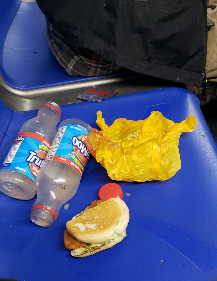 Leftover half-eaten burger and chocolate milk bottles on a bus seat, displaying messy public transport interactions.