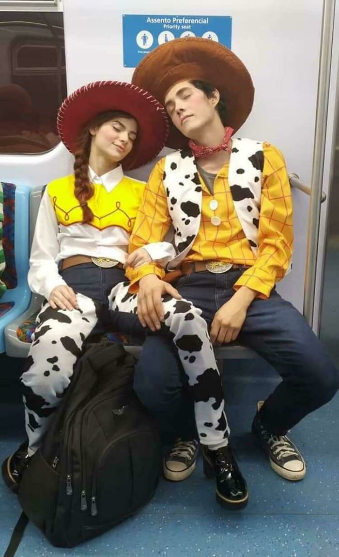 A couple dressed as Woody and Jessie from Toy Story in public transport interactions, asleep on a train.