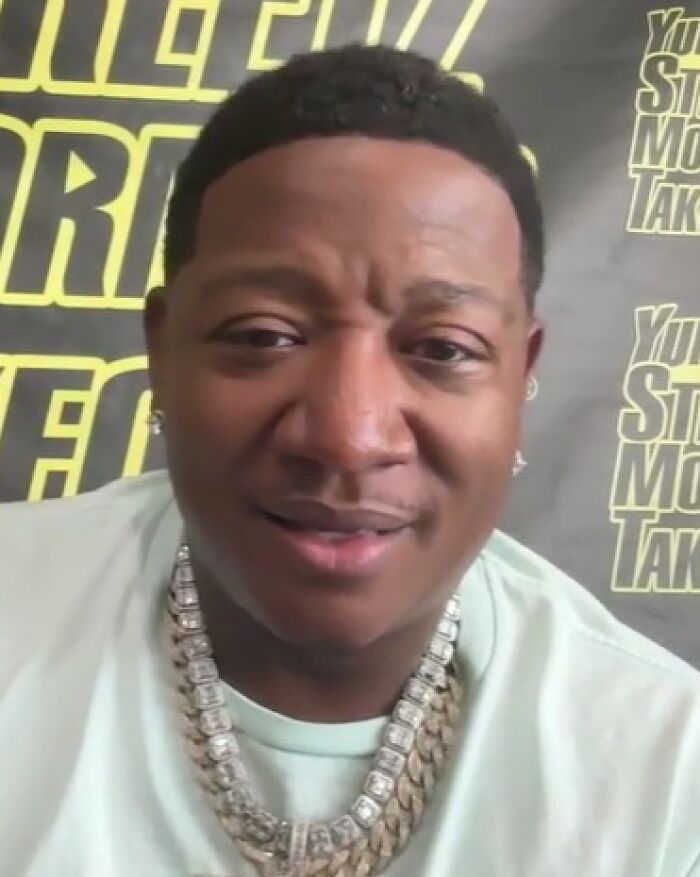 A close-up of rapper Yung Joc wearing a silver chain and smiling slightly.