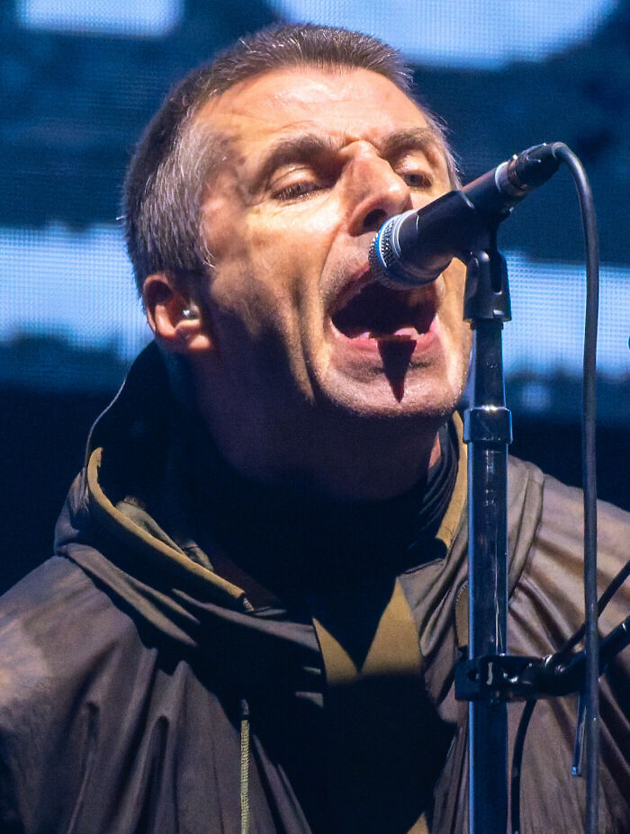 A close-up of musician Liam Gallagher singing passionately into a microphone during a live concert performance