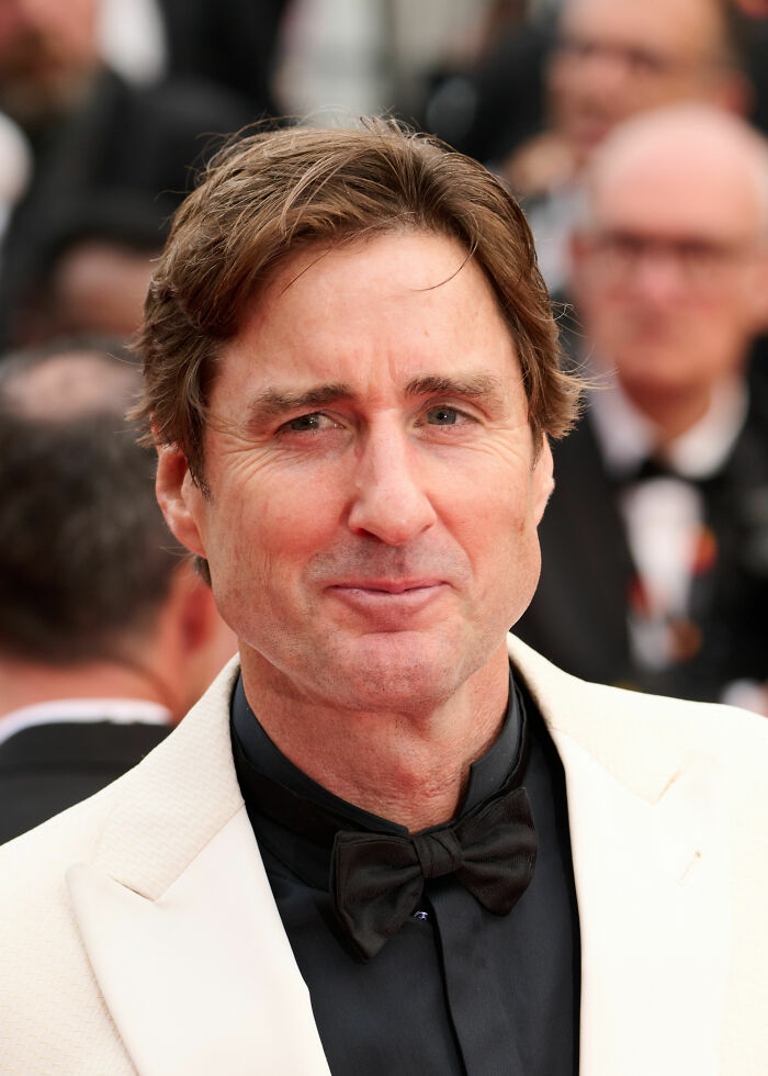 A close-up portrait of actor Luke Wilson wearing a white tuxedo and black bow tie at a red carpet event