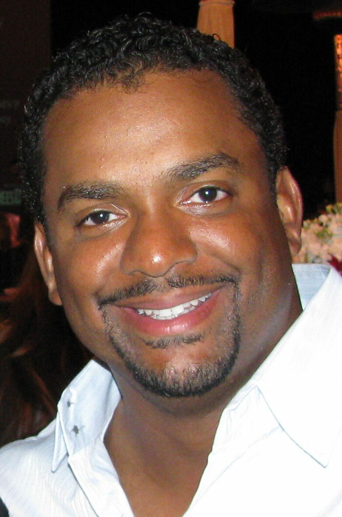 A close-up headshot of actor Alfonso Ribeiro smiling in a white shirt, showcasing his career highlights
