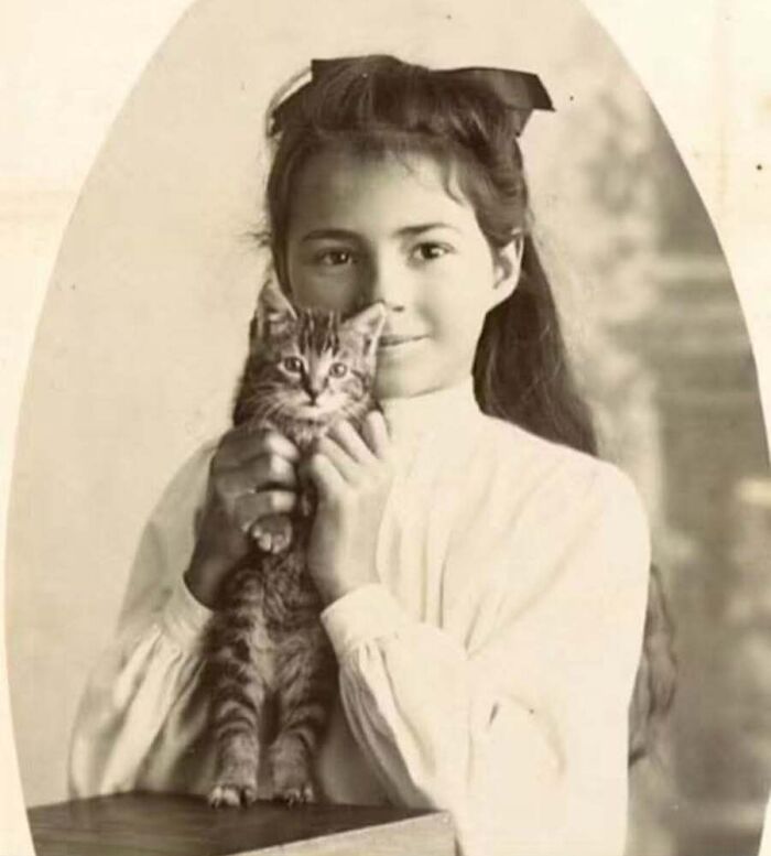 A young girl in a white dress gently holding a small kitten in a sepia-toned vintage cat photo