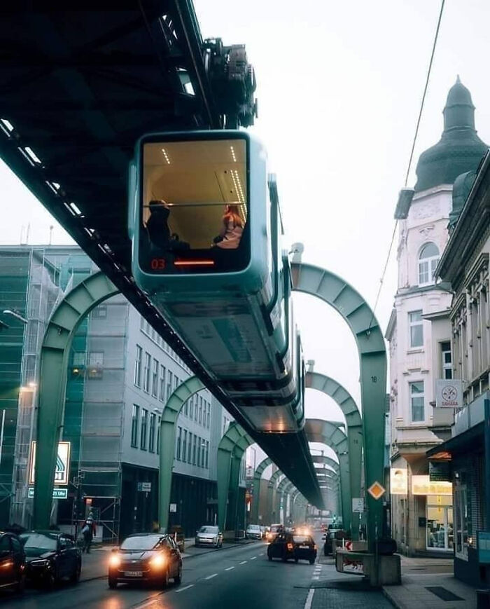 A suspended monorail train moving above a city street with cars, showcasing modern urban infrastructure.